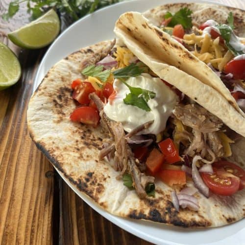 taco with carnitas, sour cream, tomatoes, onions, cilantro in a flour tortilla on a plate