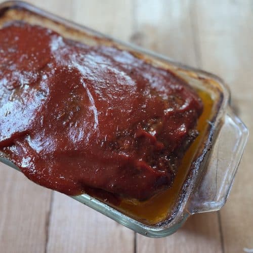 cooked meatloaf in glass loaf pan with sauce