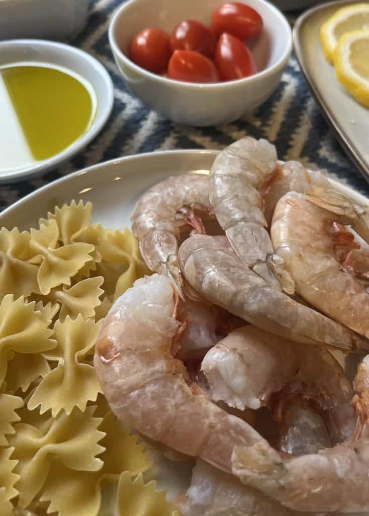 raw shrimp in shells next to dried bow tie pasta