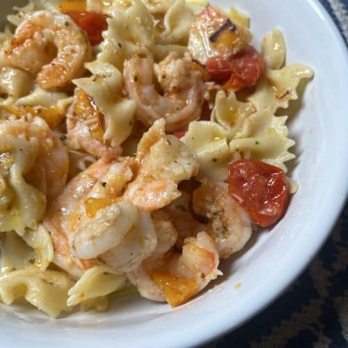 Shrimp with bow tie pasta, peppers, and tomatoes in a white bowl