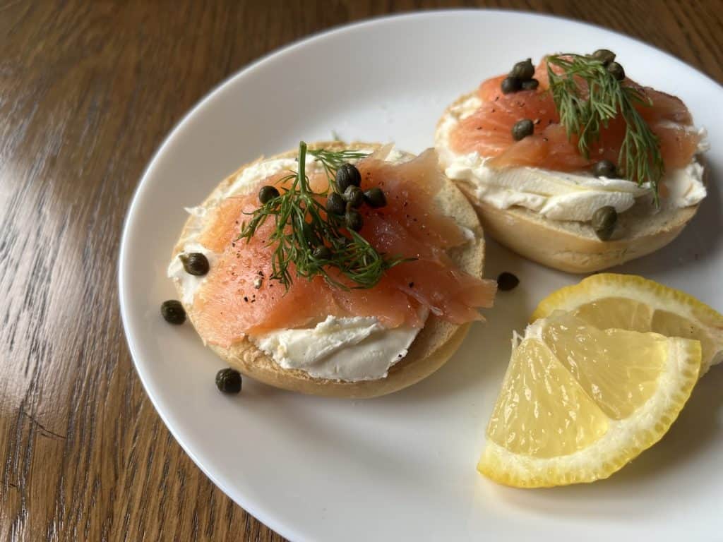 smoked salmon on a cream cheese bagel, with capers and lemon wedges on white plate