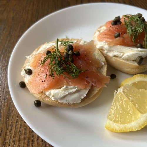 smoked salmon on a cream cheese bagel, with capers and lemon wedges on white plate