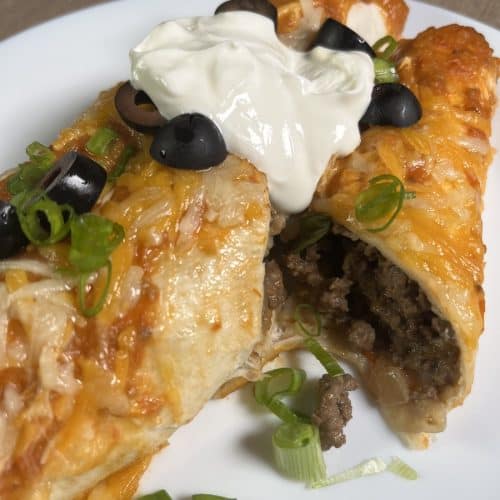 enchiladas with green onions, sour cream and black olives on a white plate