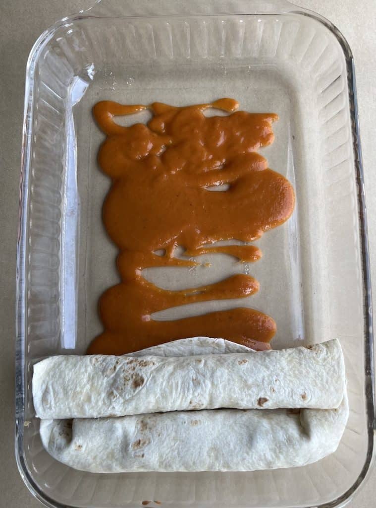 sauce and enchiladas in a casserole dish to make Beef Enchiladas with Flour Tortillas