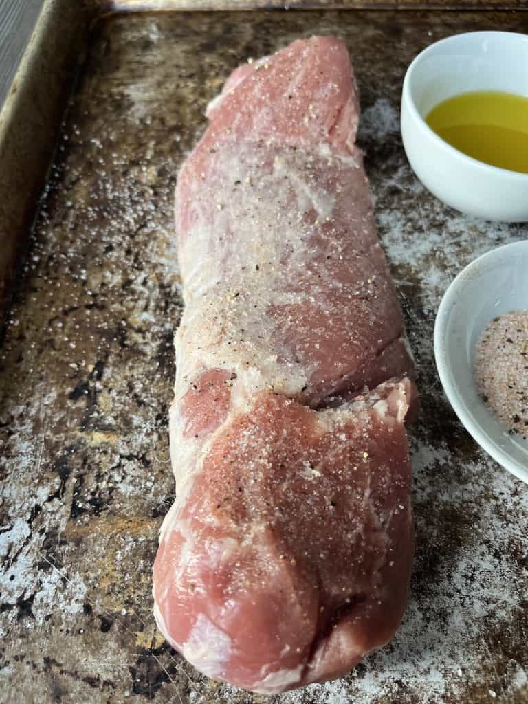 salt and pepper covered pork tenderloin on baking sheet with oil and salt and pepper in bowls