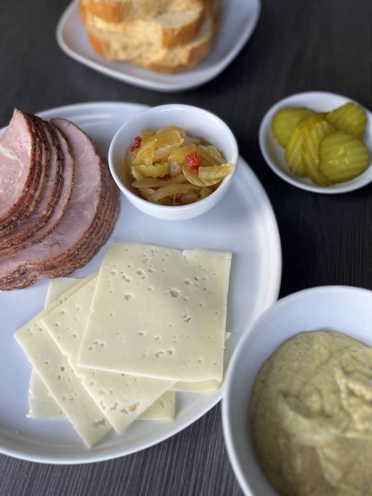 ham, cheese, onions, pickles, mustard and bread on white dishes