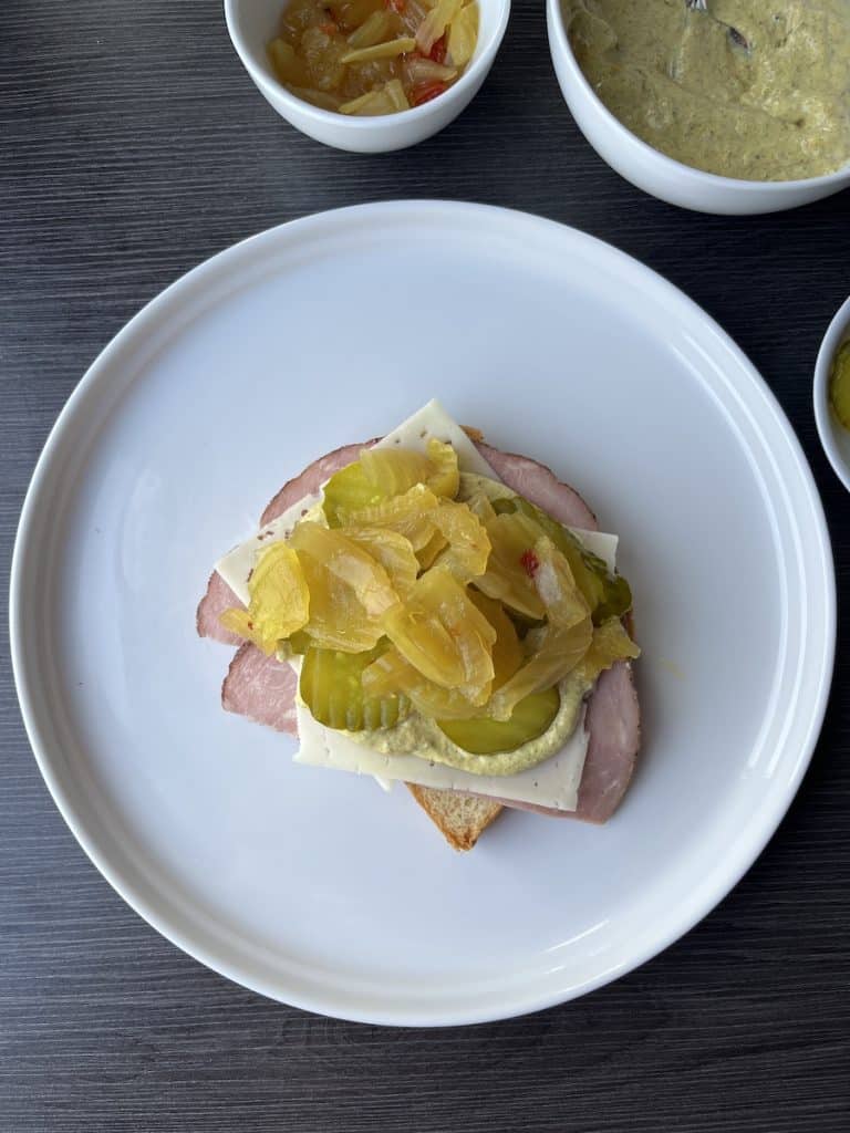 bread, ham, cheese, sauce, pickles, and onions on white plate