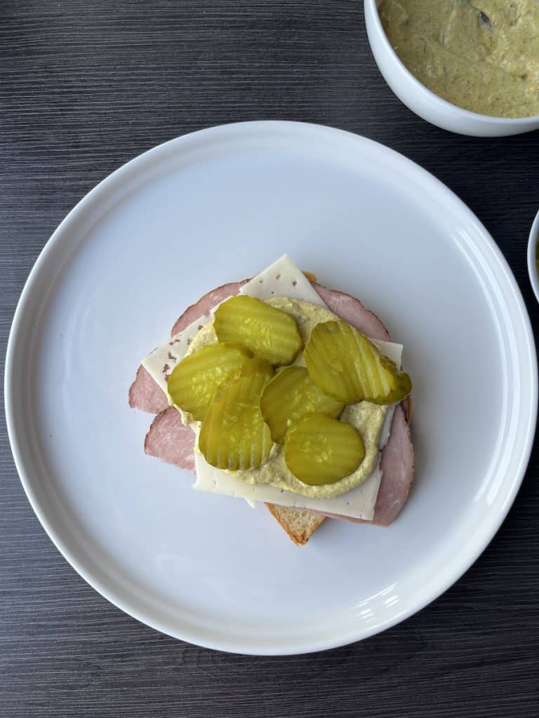 bread, ham, cheese, sauce, and pickles on white plate