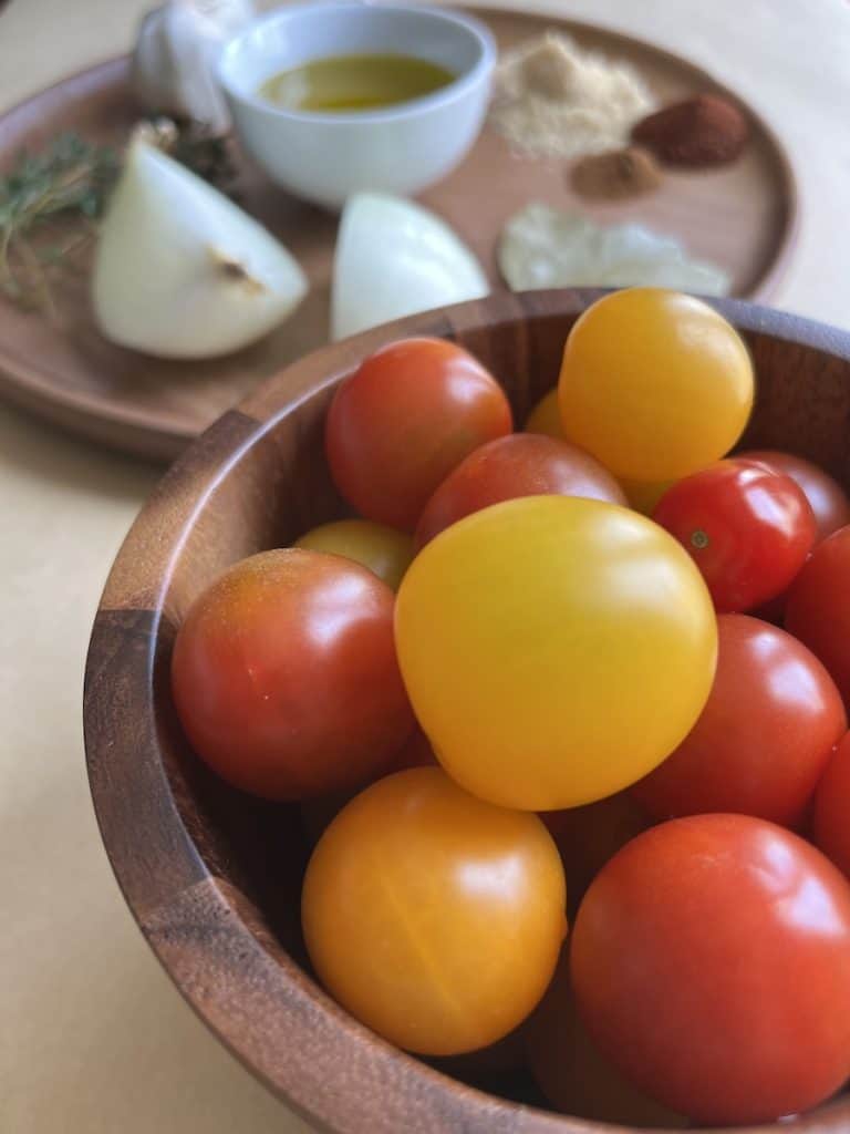 cherry tomatoes in a wooden bowl, onions, spices and oil in the background