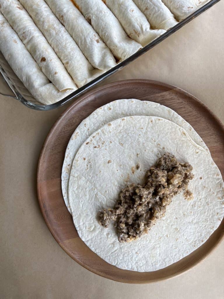 ground beef on a tortilla on a wooden plate to make Beef Enchiladas with Flour Tortillas