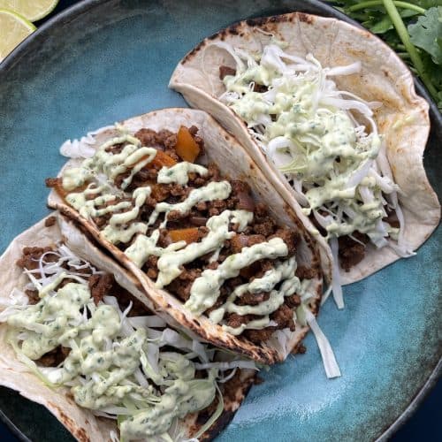 ground beef tacos with avocado cilantro aioli sauce on flour tortillas with lime wedges