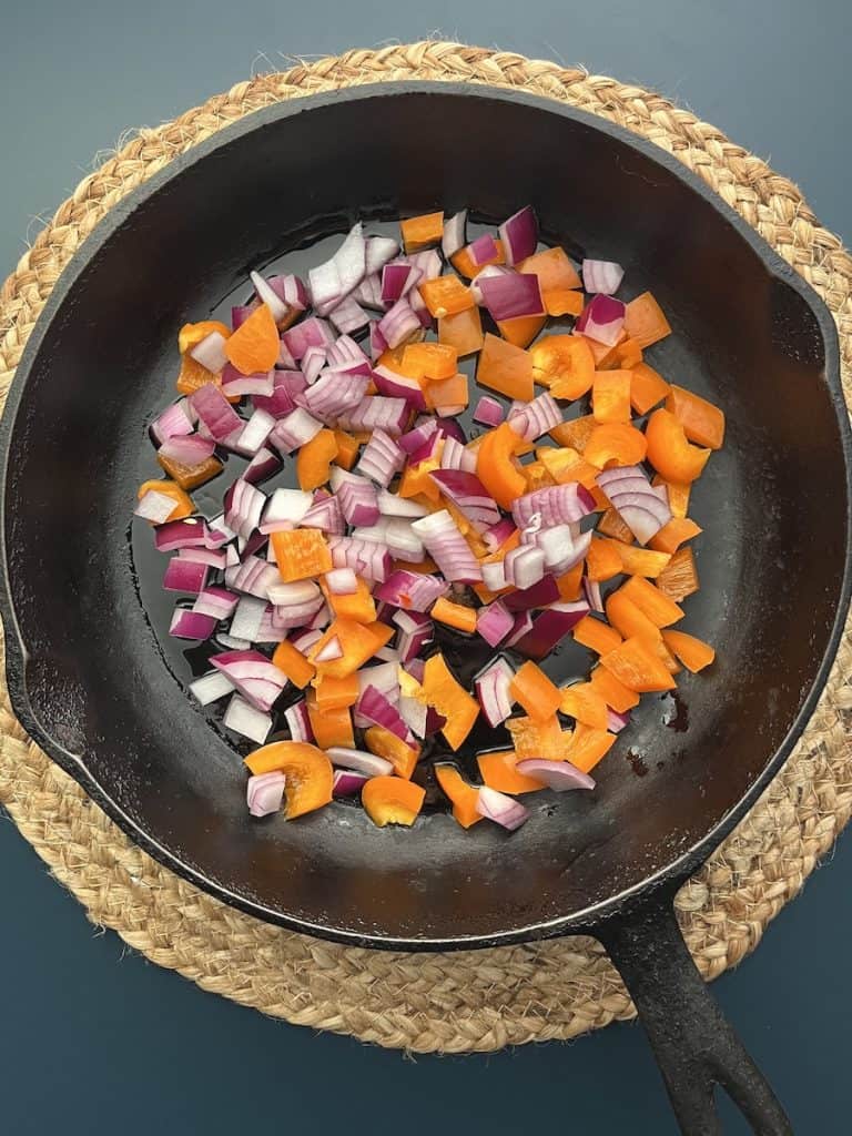 chopped red onions and orange peppers in cast iron skillet