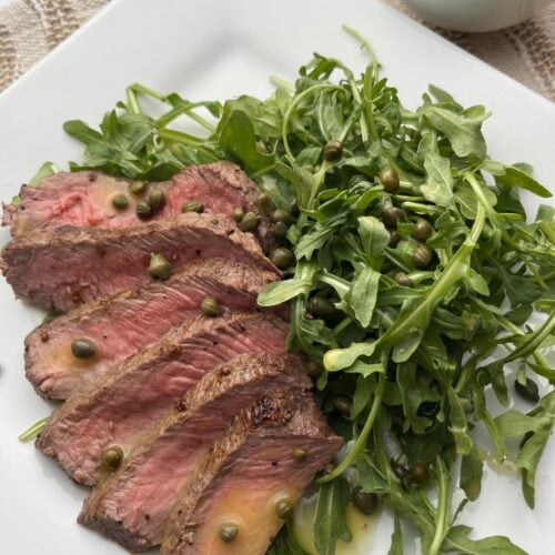 arugula steak salad with capers, lemon vinaigrette dressing on a plate