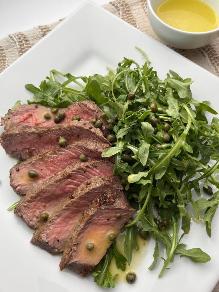 arugula steak salad with capers, lemon vinaigrette dressing on a plate
