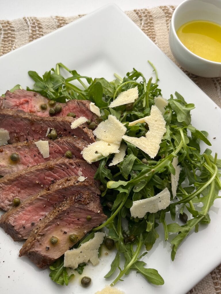 arugula steak salad with capers, lemon vinaigrette dressing and parmesan cheese on a plate
