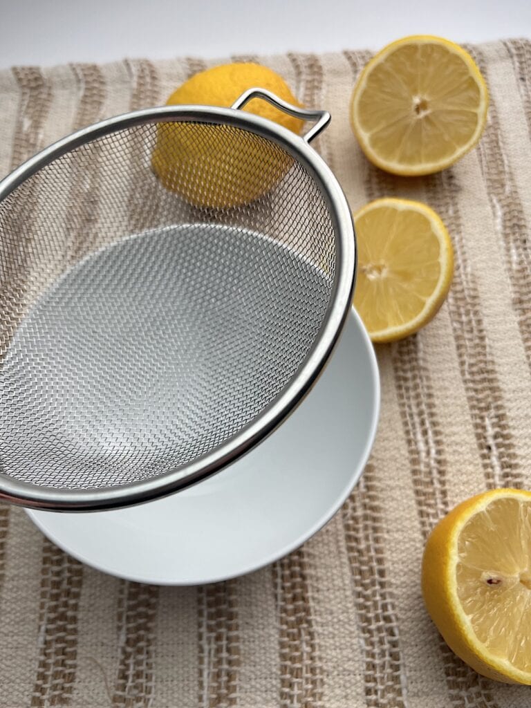small strainer over a bowl with lemons in the background