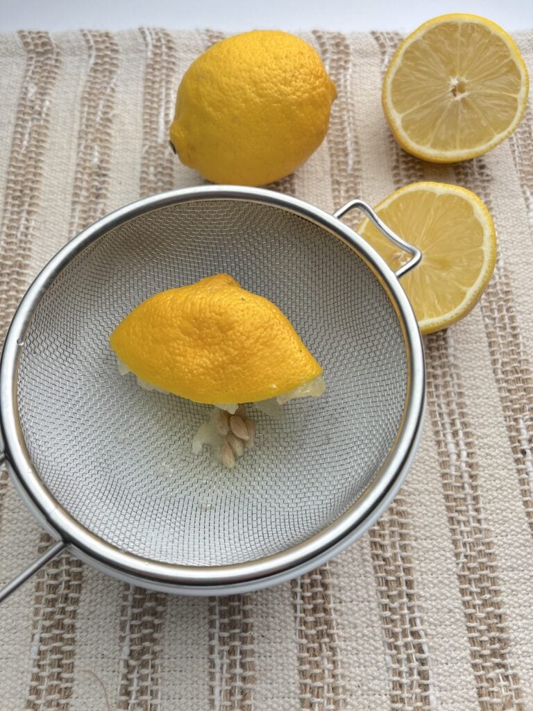 squeezed lemon in a strainer over a bowl with lemons in the background