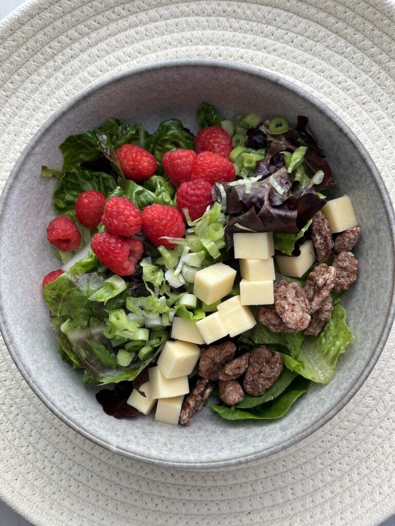 mixed salad leaves with raspberries, green onions, cubed Havarti cheese and pecans in a bowl
