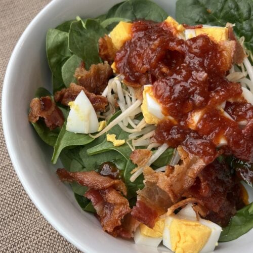 spinach salad with dressing, eggs, bacon and sprouts