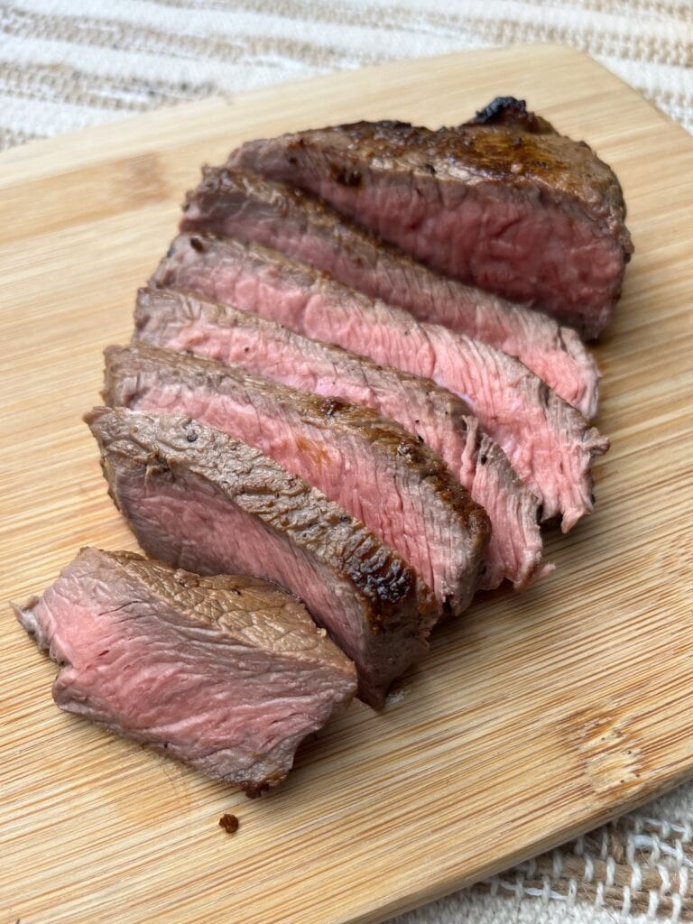 cooked and sliced top sirloin steak with salt and pepper on a wooden plate