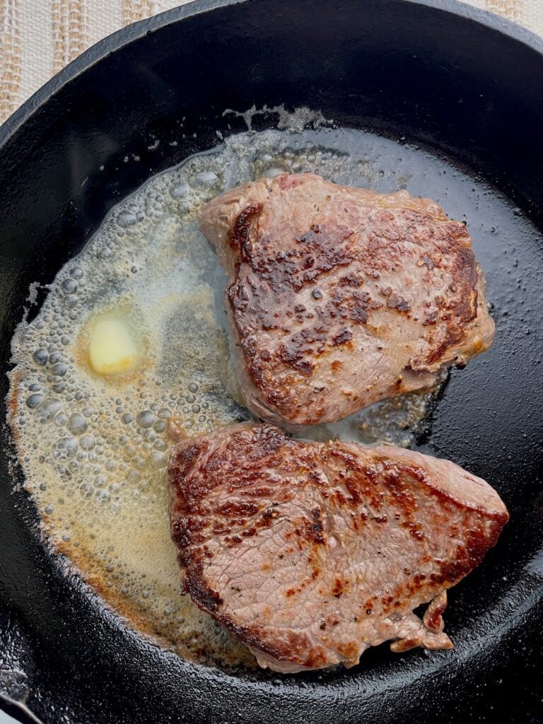 cooked top sirloin steak with salt and pepper with butter in a cast-iron skillet