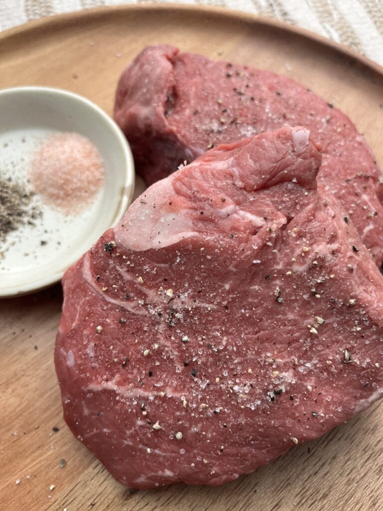 raw top sirloin steak with salt and pepper on a wooden plate