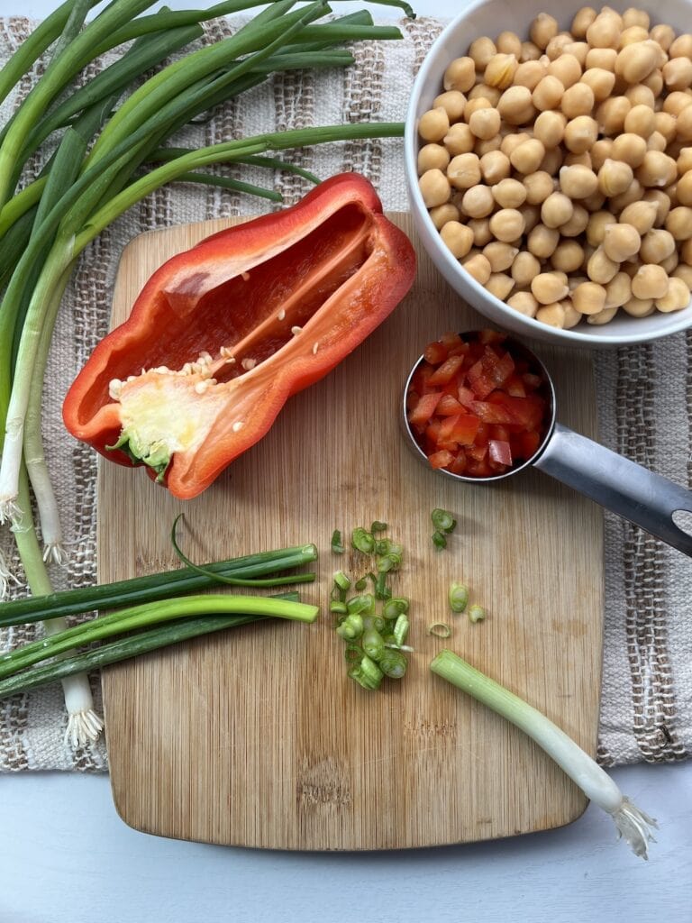 green onions and red peppers on a cutting boards, chickpeas in a bowl, green onions on the side