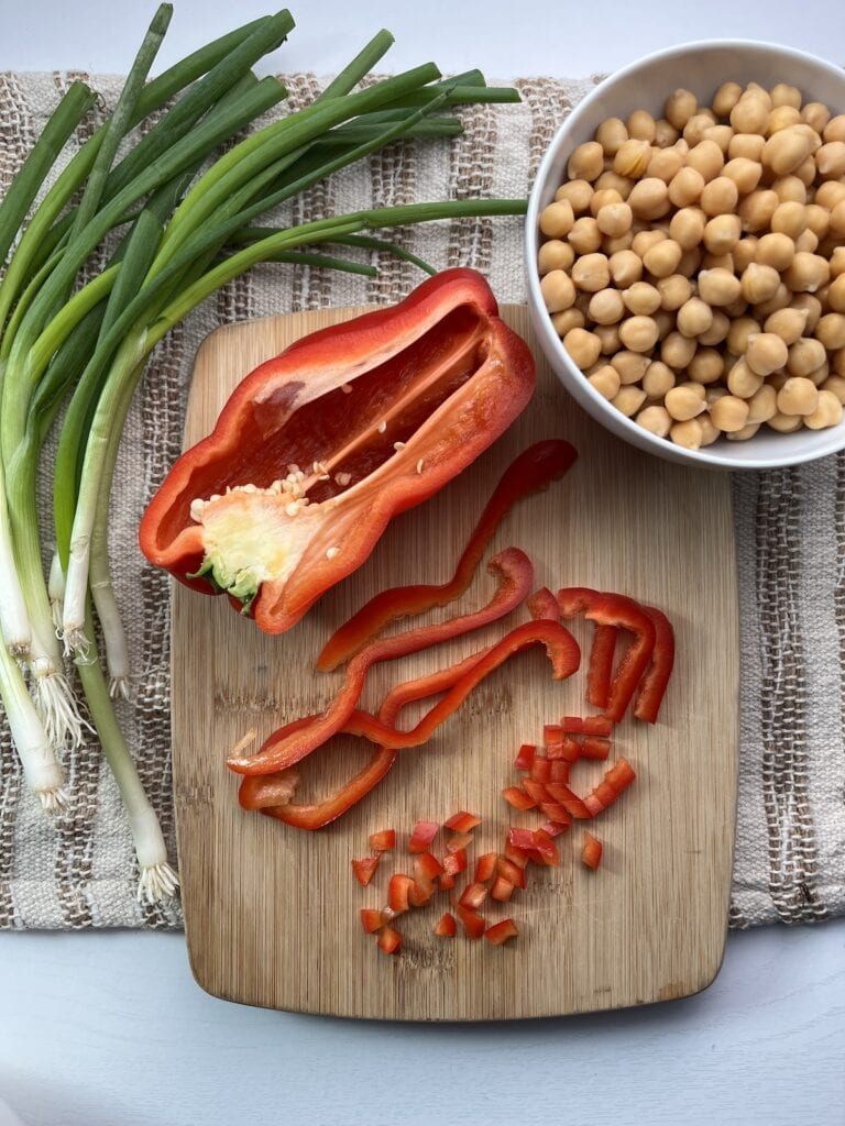 red peppers on a cutting boards, chickpeas in a bowl, green onions on the side