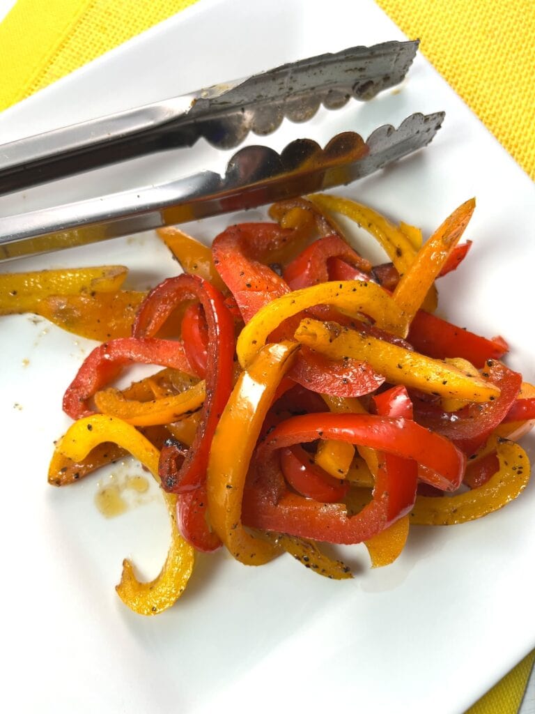 sauteed bell peppers with lemon pepper seasoning on plate with tong