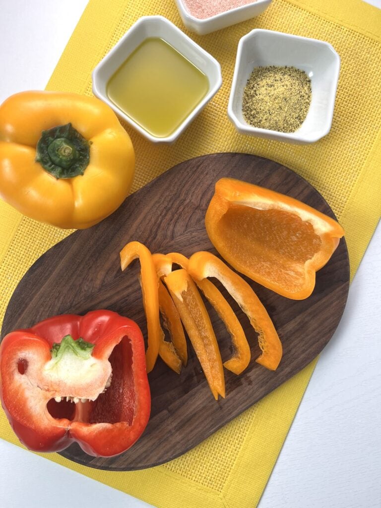 sliced orange bell pepper, red pepper, and yellow whole peppers, oil, salt and seasoning in bowls