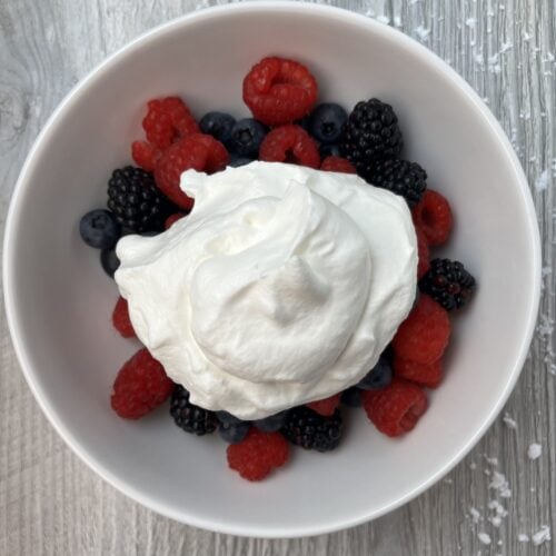 whipped cream over mixed berries in a bowl