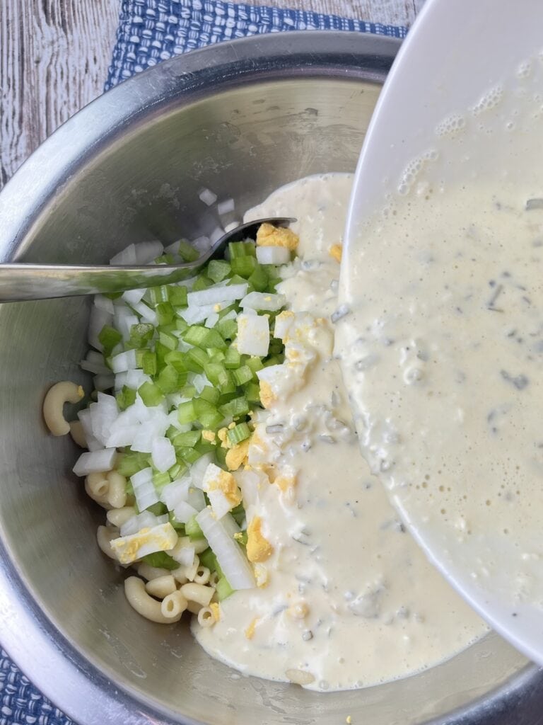 pouring the dressing over the celery, onions, and cooked pasts