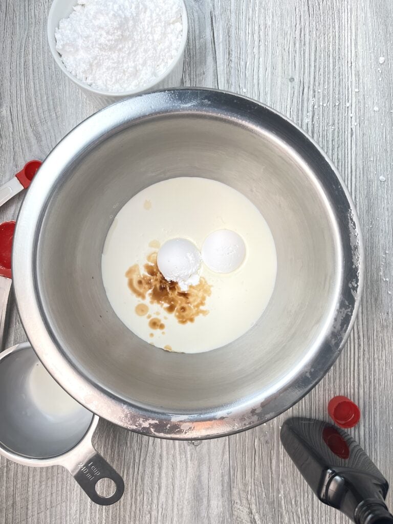 vanilla in a bowl of heavy whipping cream with two scoops of powdered sugar