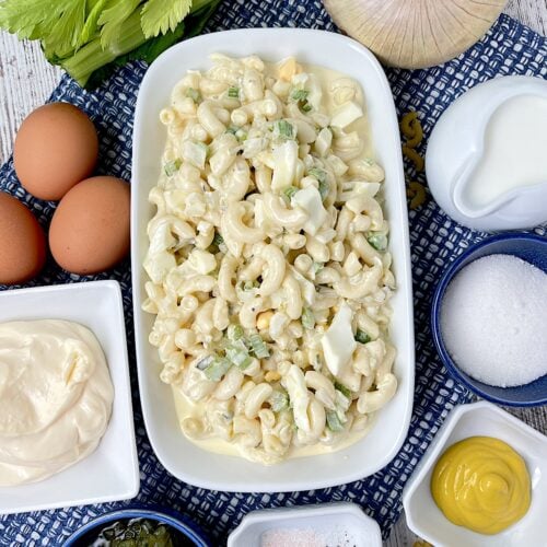 deli stile macaroni salad in a bowl with the ingredients around it in smaller bowls