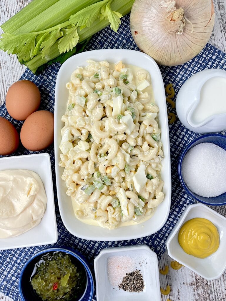 deli stile macaroni salad in a bowl with the ingredients around it in smaller bowls