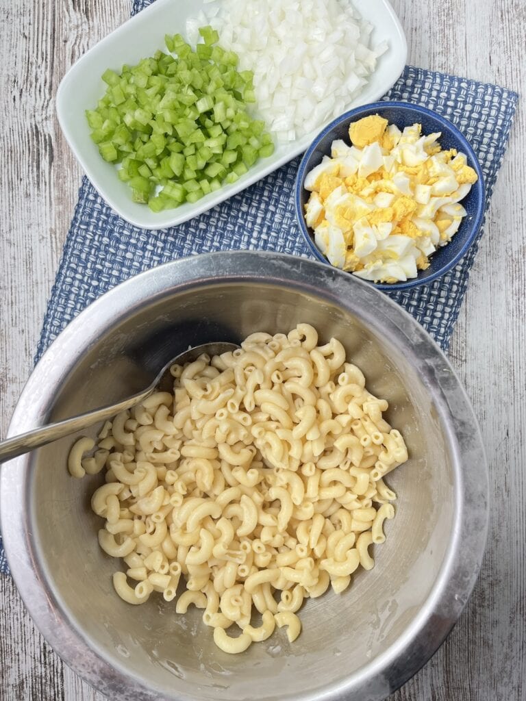 cooked pasta in a metal bowl, celery, onions, eggs in small bowls