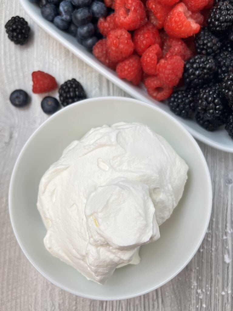 mixed berries on a plate with a bowl of whipped chantilly cream