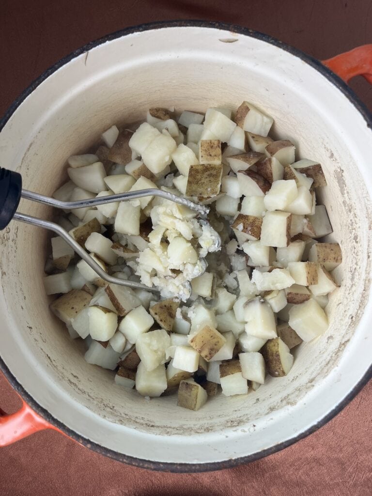 cooked potatoes in a stock pot with a potato masher