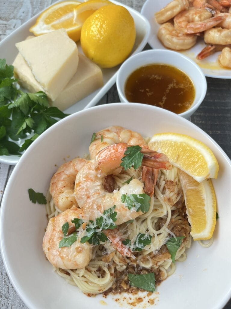 shrimp scampi with sauce over angel hair pasta, parsley, lemons and grated parmesan cheese