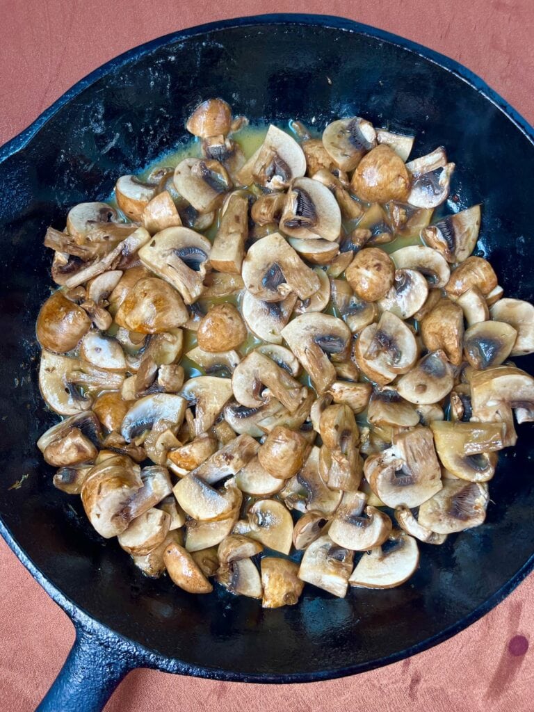 half cooked mushrooms in butter in a skillet